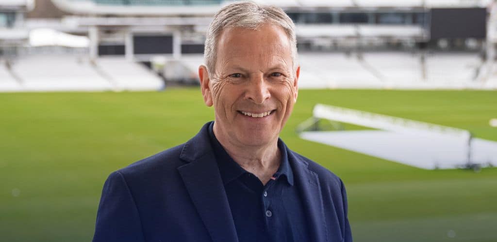 Smiling man in a suit stands in front of a sports field.
