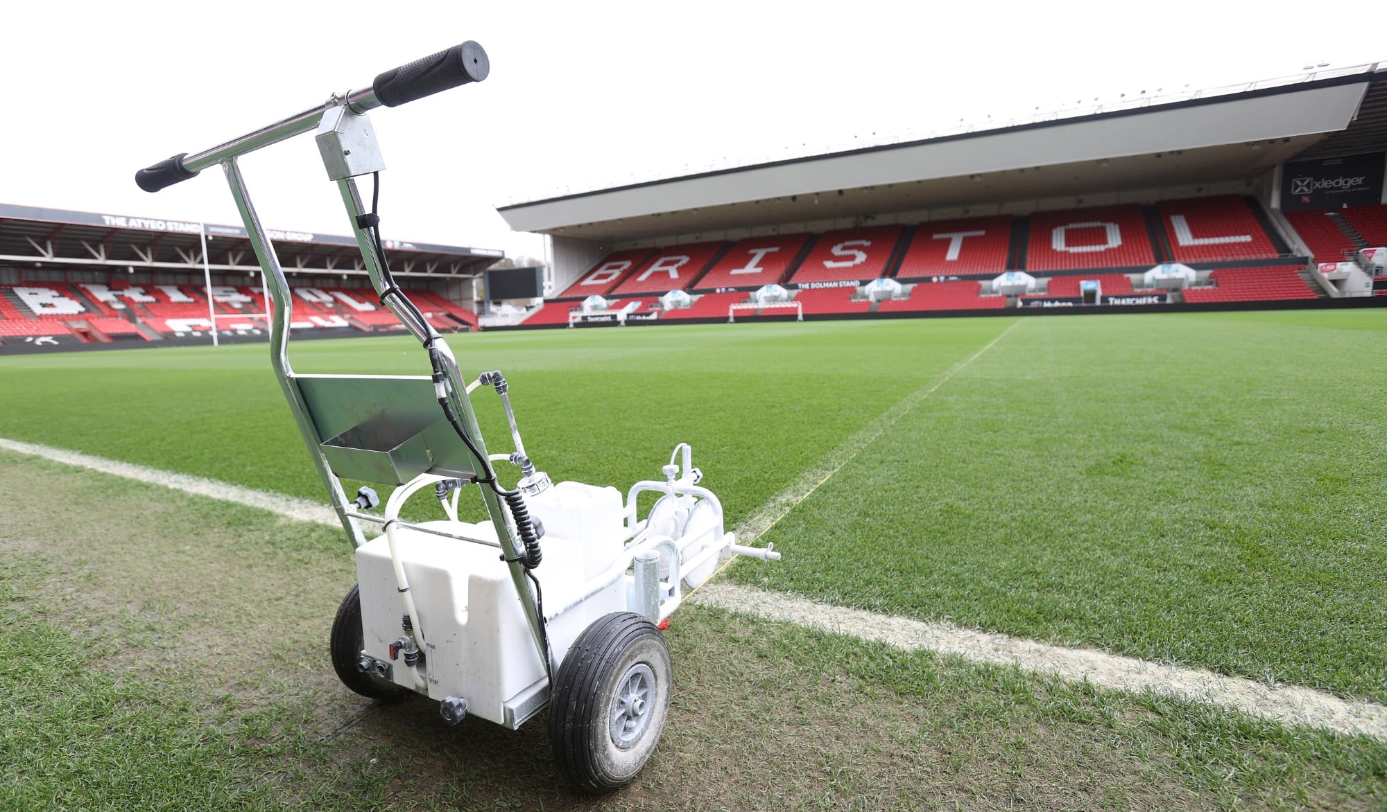 A line marking machine on the edge of a football field in a stadium.