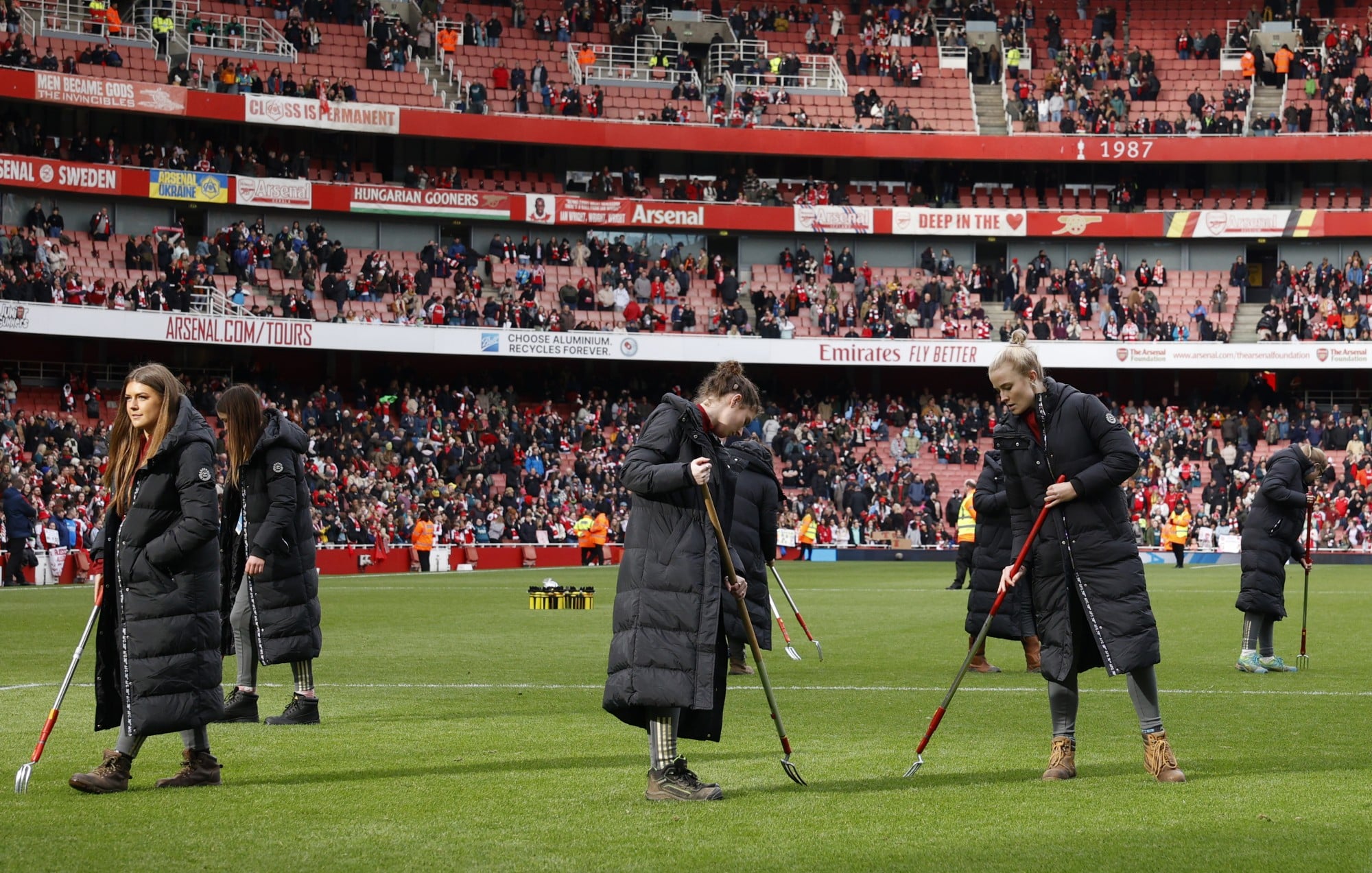 People cleaning the football field with brooms while fans watch from the stadium seats.