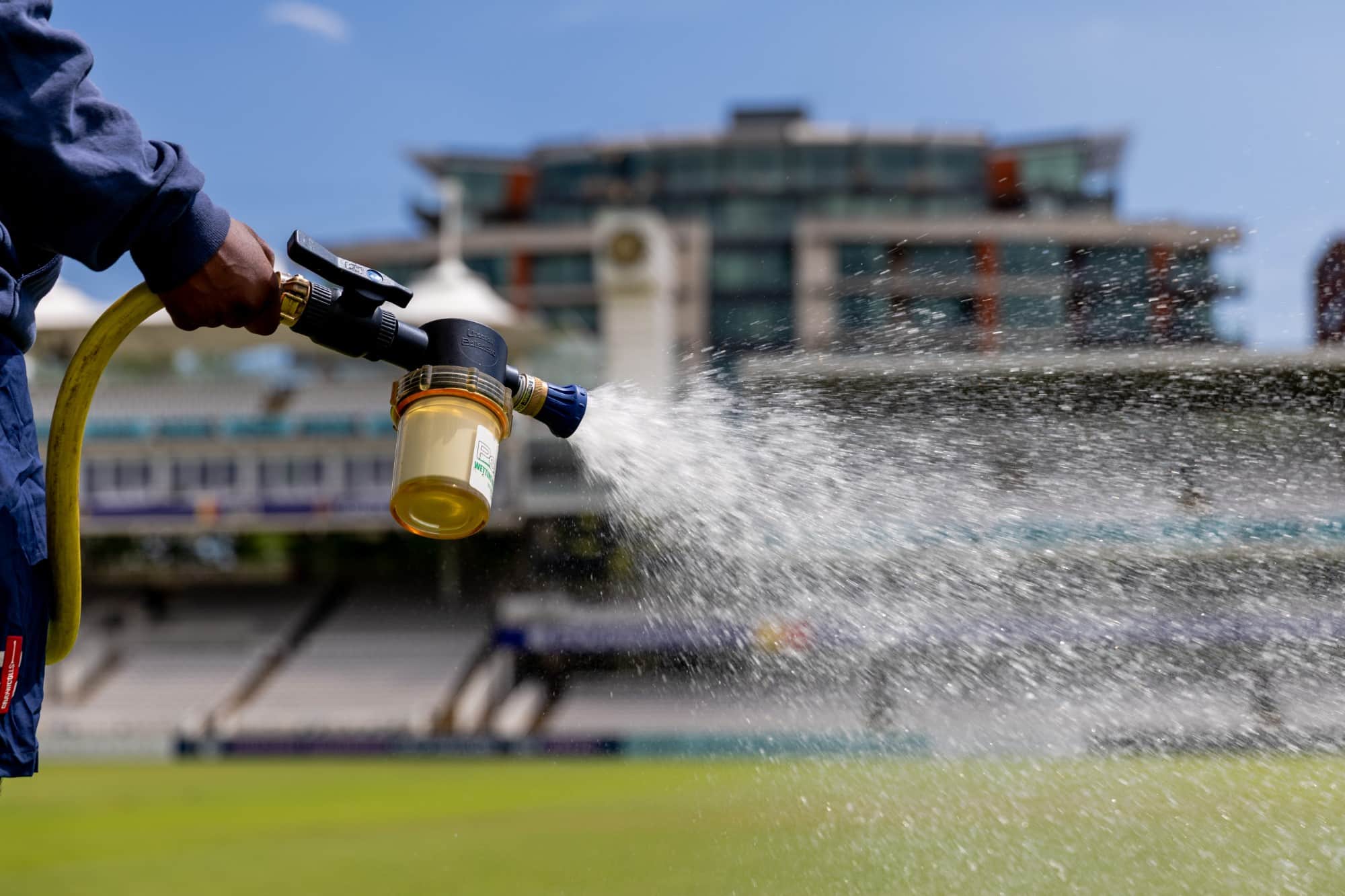 DavidHemstock A person sprays water on grass at a sports stadium with a hose and nozzle.
