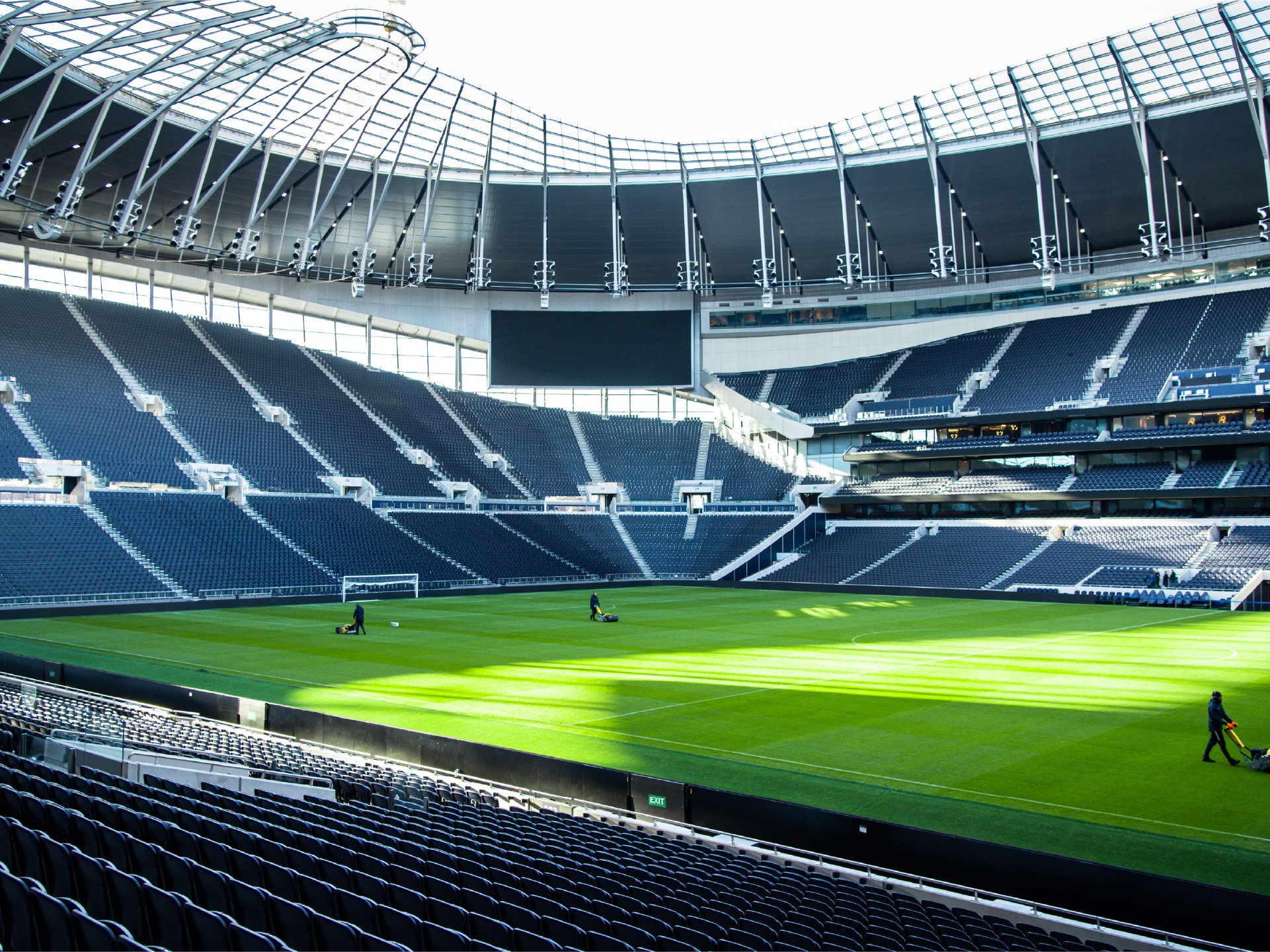 Maintenance-funding-football Empty football stadium with green field and a few people working on the pitch.